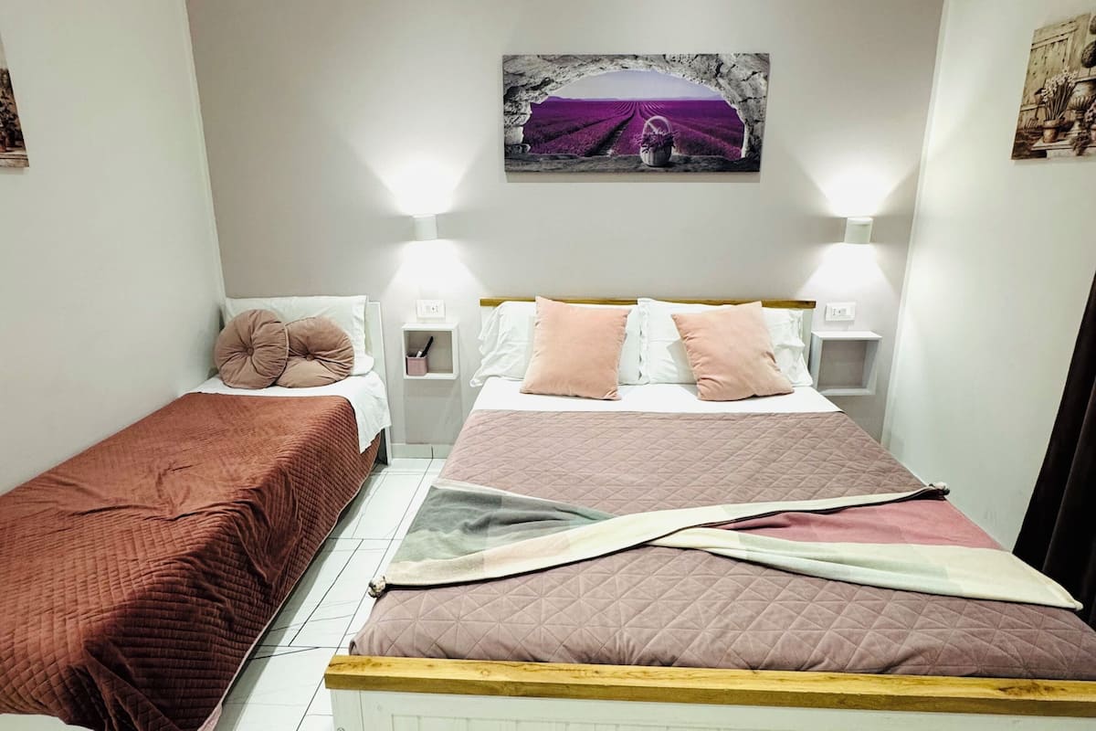 A bedroom with two beds, a white wall, and a ceiling light fixture.
