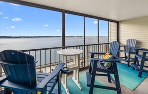 Een balkon met uitzicht op een groot wateroppervlak, voorzien van blauwe Adirondack stoelen en een kleine tafel.
