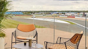 A terrace with two wire mesh chairs and a table, overlooking a race track.