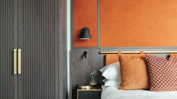 A modern hotel room with a dark wood wardrobe, a bedside table with a lamp, an hourglass, and a patterned throw blanket.