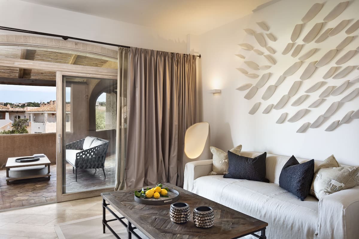 Ein modernes Wohnzimmer mit einer Couch, einem Couchtisch und einem Esstisch. Es gibt einen Balkon mit Stuhl und Tisch, sowie eine Wand mit Dekorationselementen.