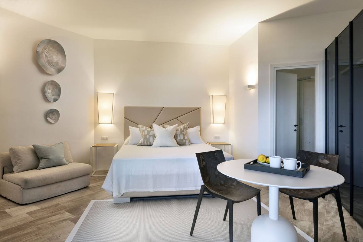 Ein modernes Hotelzimmer mit Bett, einer Couch, einem Esstisch und einem Tablett mit Tassen und Zitronen.