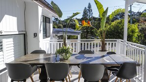 Un espace extérieur abrité, aménagé pour les repas, avec une table en bois et des chaises noires, entouré de rampes blanches et de plantes en pot.