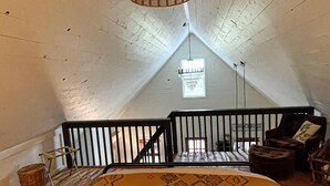 Un dormitorio acogedor en el ático, con una cama grande, una lámpara colgante de mimbre, un ventanal pequeño y vistas al cielo.