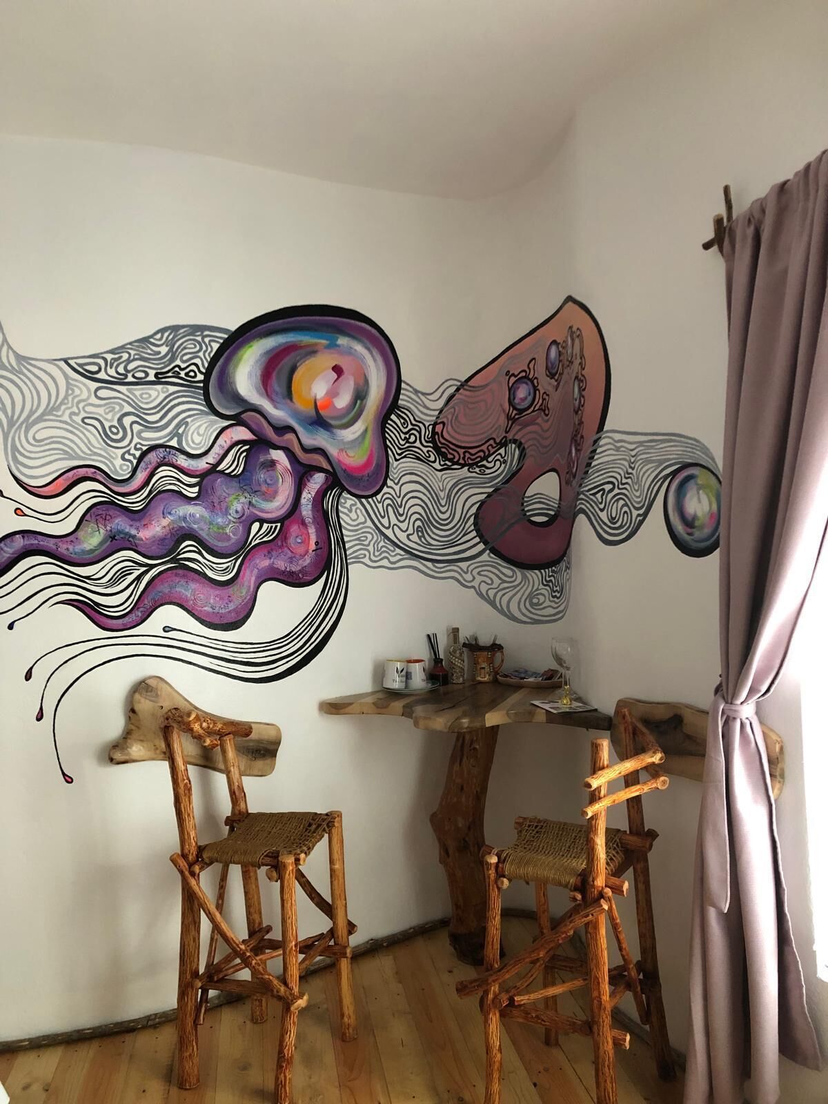 A room with a wooden dining table, two wooden chairs, and a wall mural.