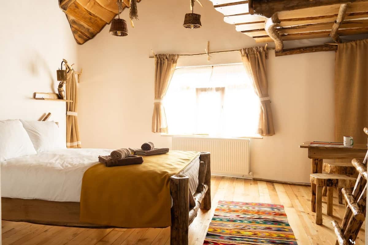 A rustic bedroom with a wooden bed, a wooden table, and a colorful rug.
