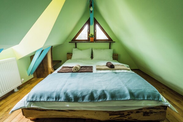A cozy attic bedroom with a sloped ceiling, a wooden bed frame, and a window with a view of the outdoors.