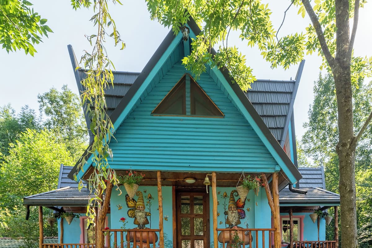 A rustic house with a steeply pitched roof, a stone foundation, and a wooden porch.