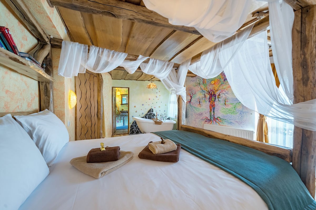 A bedroom with a canopy bed, a painting on the wall, and a view of the bathroom.