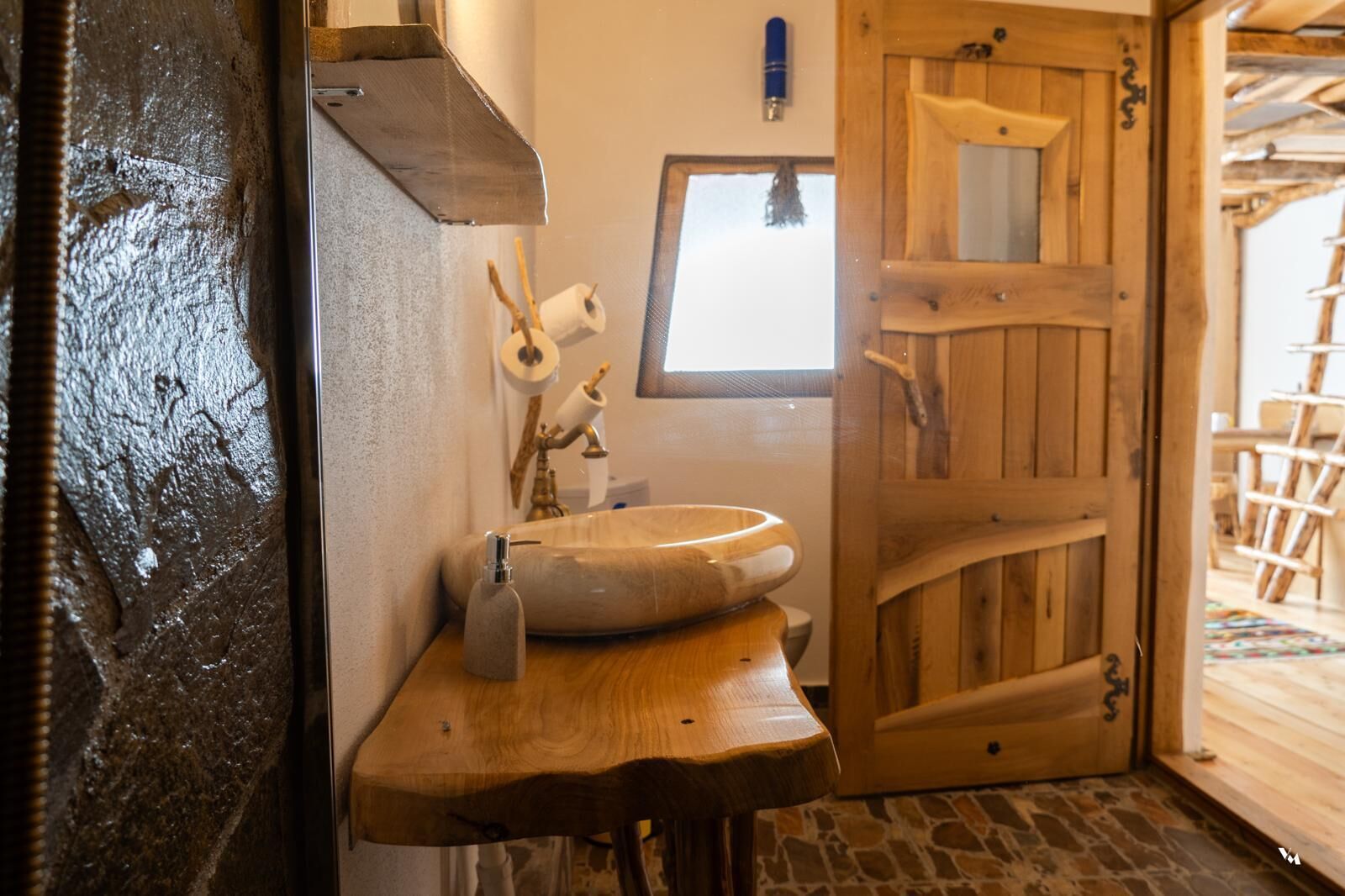 Une salle de bain rustique avec un lavabo en bois, des toilettes et une porte en bois.