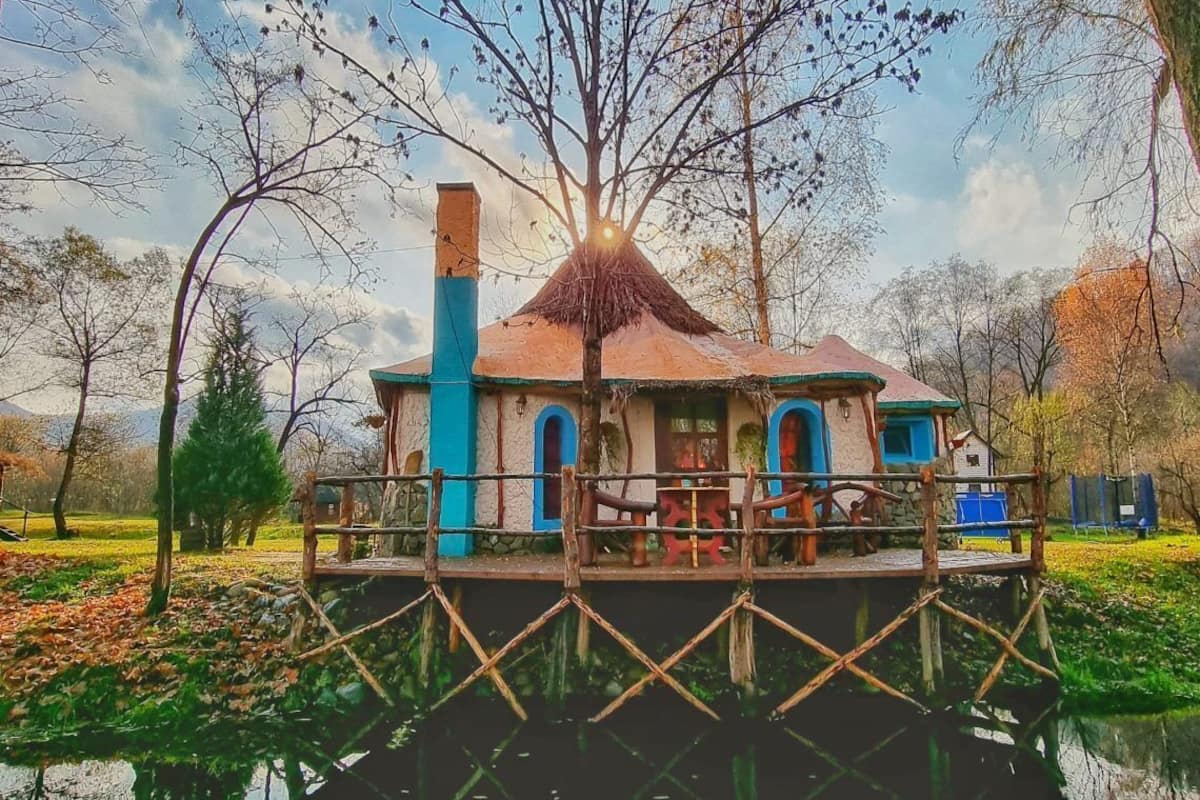 A houseboat with a thatched roof, blue and white exterior, and a dock extending into a calm body of water.
