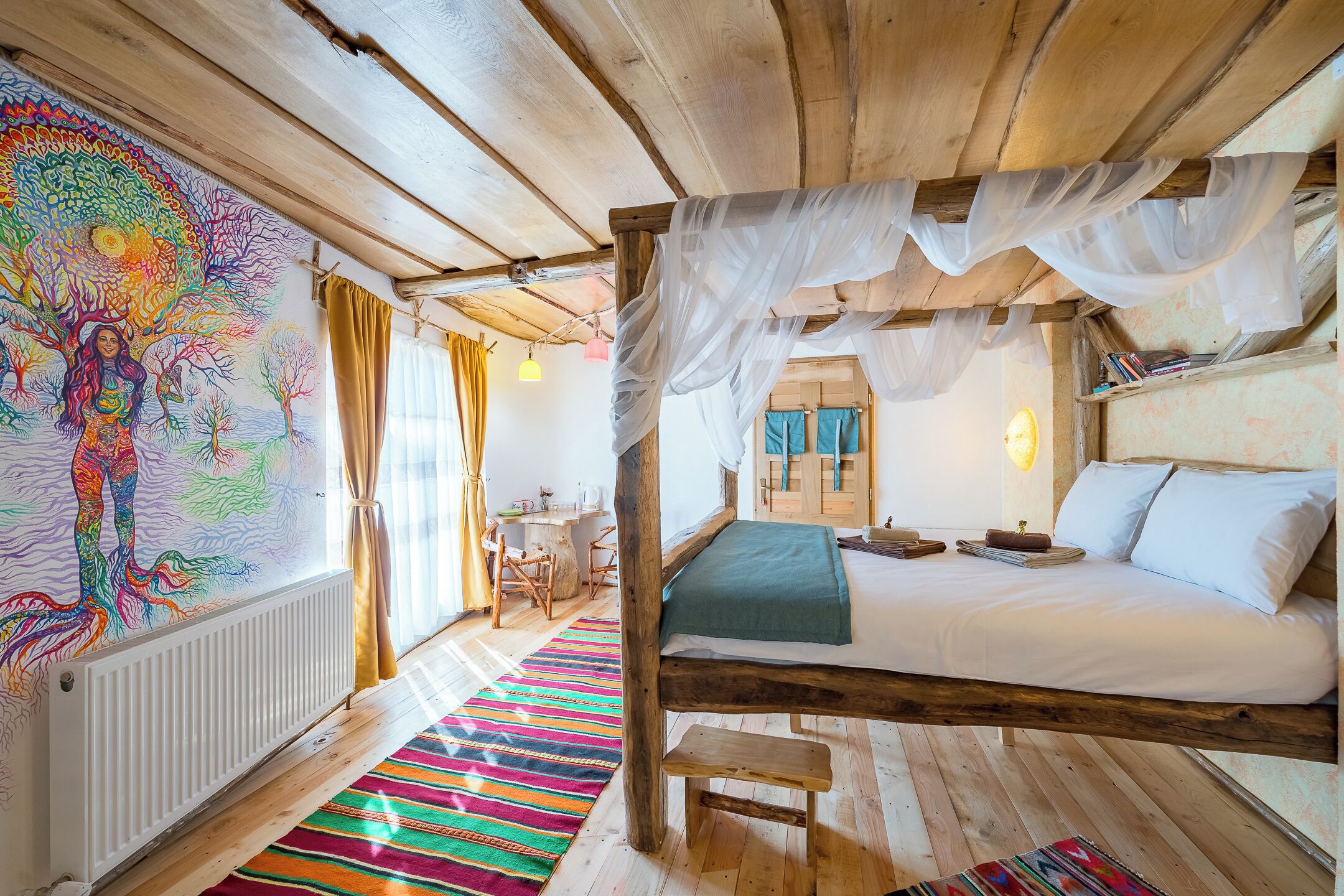 A rustic wooden room with a four-poster bed, a colorful mural, and a striped rug.