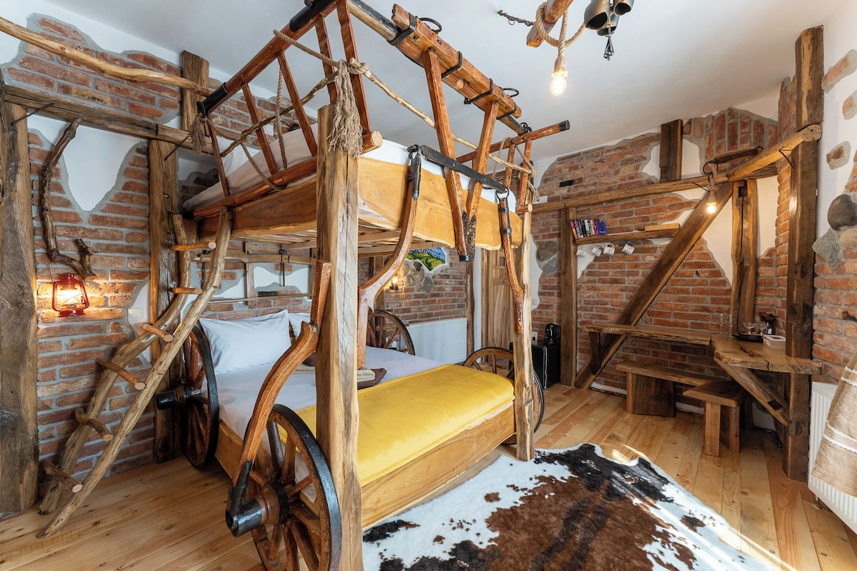 A rustic room with a wooden four-poster bed, a cowhide rug, and a brick wall.