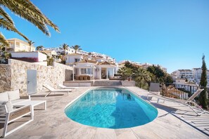 Relax by the pool surrounded by a stone wall and lounge chairs.
