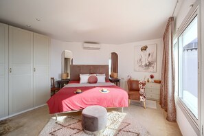 Cozy retreat with a large bed, nightstand, and chair, plus a wardrobe and framed artwork.