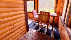 Interior de una cabaña de madera con una mesa de comedor y sillas, una ventana con vista a árboles, y piso de madera.
