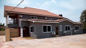 A two-story house with a tiled roof, multiple windows, and an air conditioning unit on the exterior wall. - Hotel Lily  (Santeo)