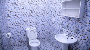 A bathroom with a toilet and sink, both white, against a blue and brown speckled tile wall. - Hotel Lily  (Santeo)