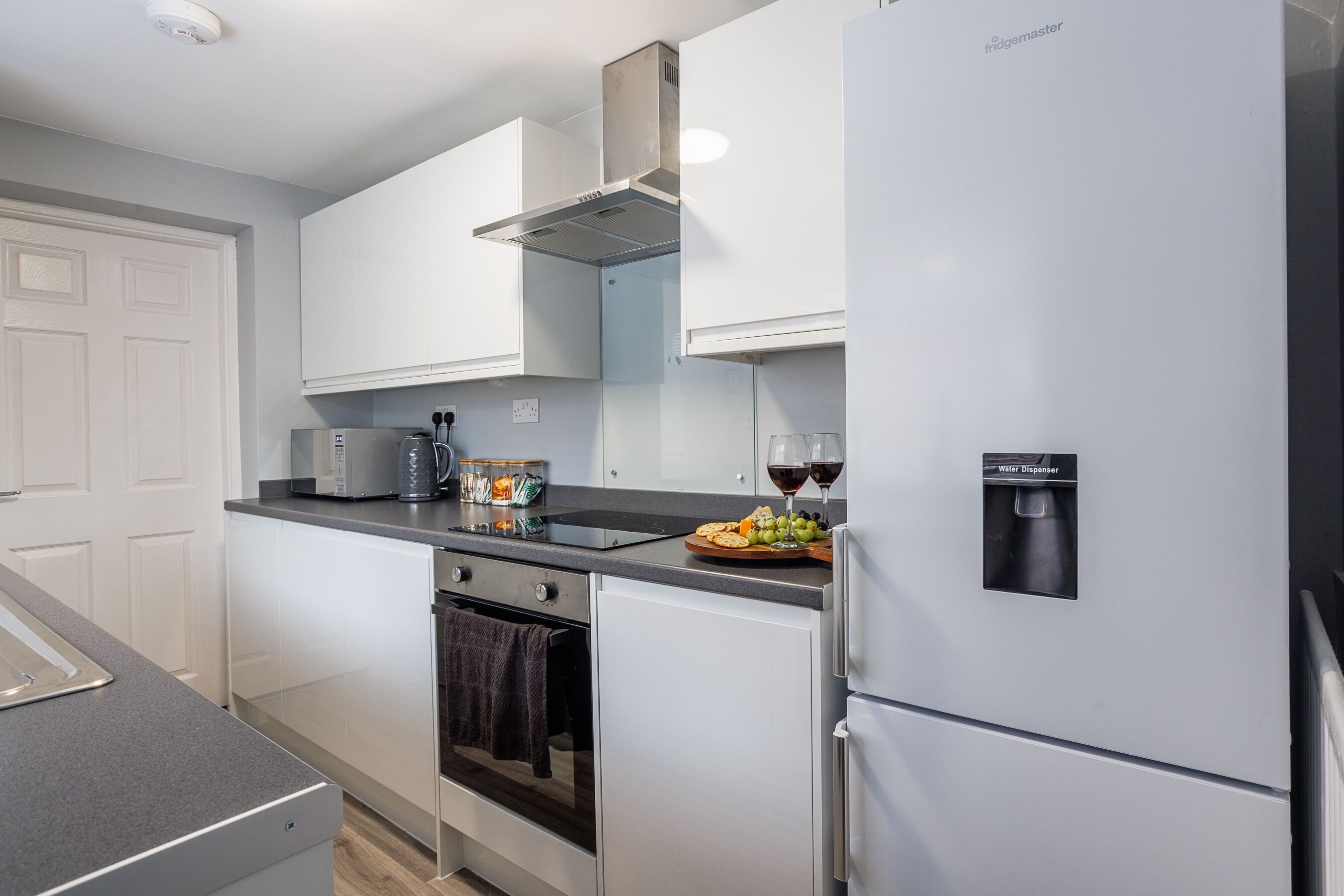 A modern kitchen with white cabinets, a stainless steel refrigerator, a built-in oven, and a microwave.