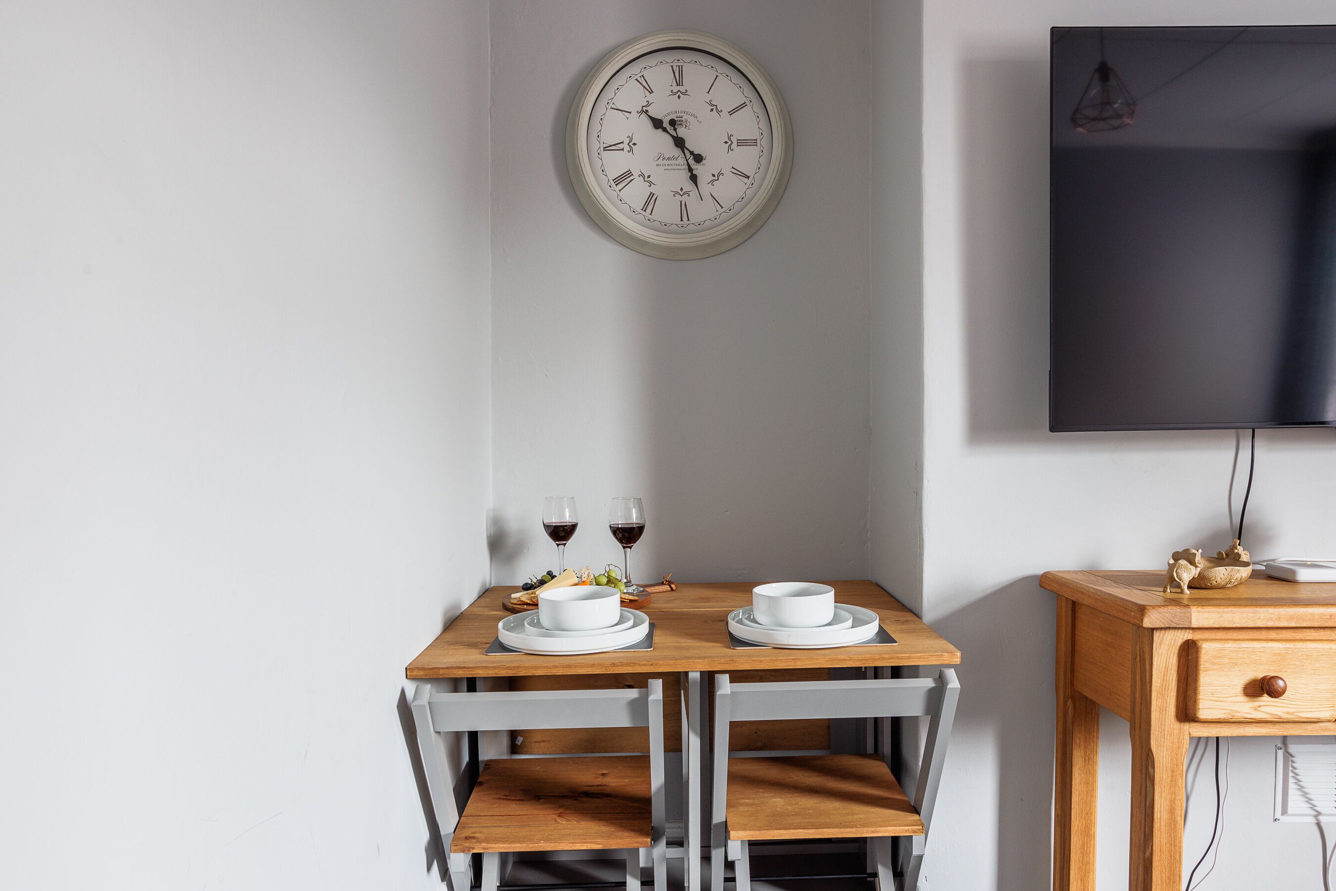 Une table à manger avec deux assiettes blanches, deux verres à vin et un saladier de fruits.