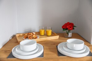 En frukostuppsättning med croissanter, apelsinjuice och en vas med röda rosor på ett träbord.