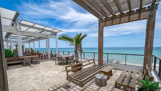 Un patio al aire libre con mobiliario de madera, una palmera y vista al océano.