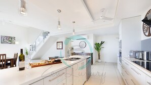 A modern kitchen with white cabinetry, a central island, and stainless steel appliances. - Zen Ocean View Ph Spacious Living Pool Parking (Darwin)