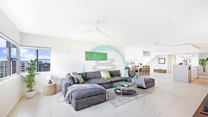 A modern living room with a grey sectional sofa, a round coffee table, and a dining area with a white cabinet and chairs. - Zen Ocean View Ph Spacious Living Pool Parking (Darwin)