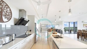 A modern kitchen with white cabinetry, a central island, and pendant lighting. - Zen Ocean View Ph Spacious Living Pool Parking (Darwin)