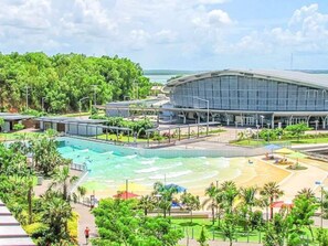 Un hotel moderno con una piscina grande, zona de playa y abundante vegetación.