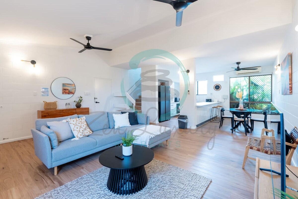 A modern living room with a sofa, coffee table, and a dining area with chairs and a table.