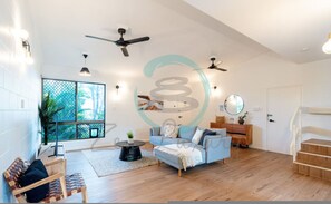 Ein geräumiges Wohnzimmer mit großem Fenster, einem blauen Sofa, einem Holztisch und einer Treppe.
