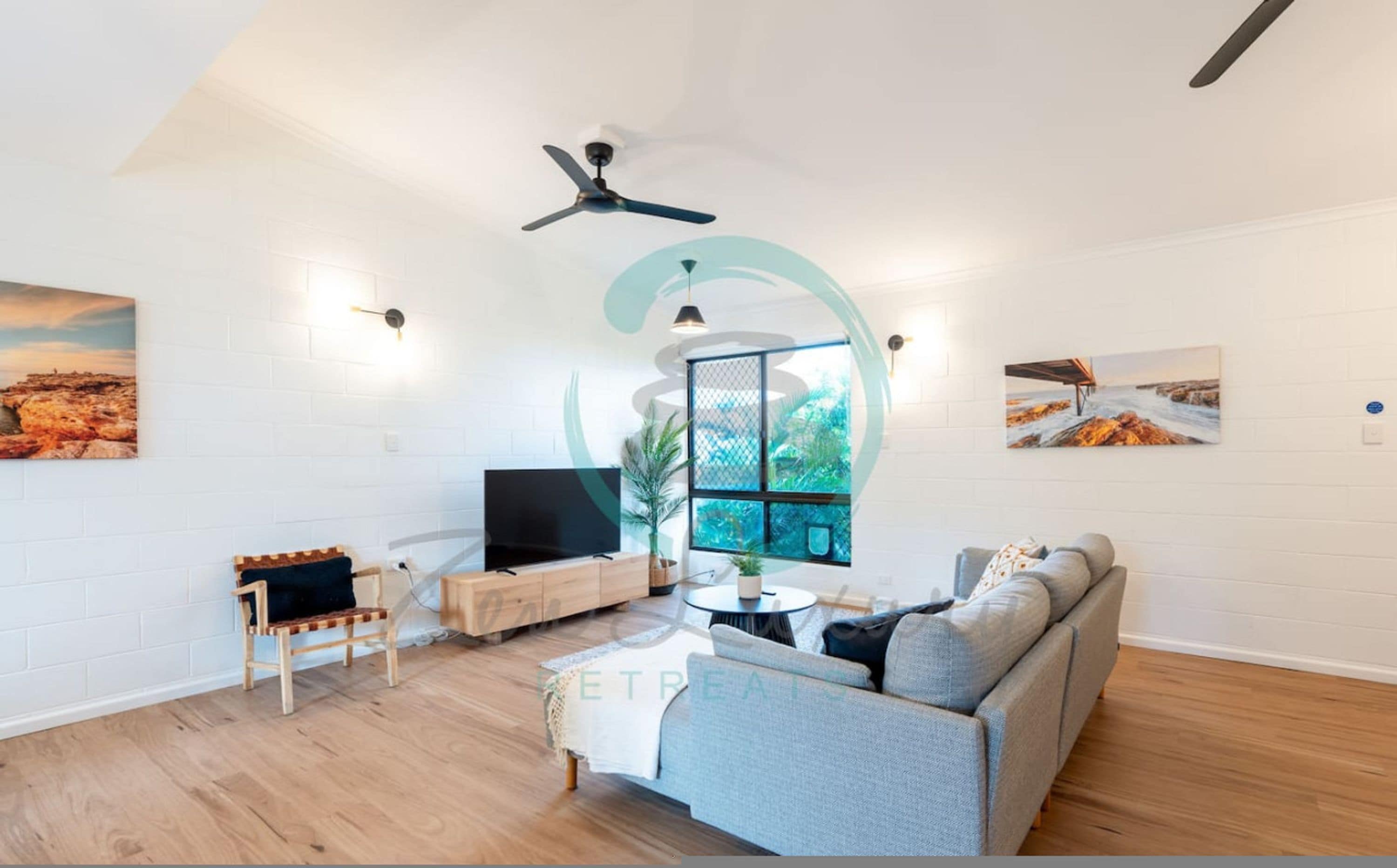 Ein modernes Wohnzimmer mit einer Couch, einem Fernseher, einem Deckenventilator und Kunstwerken an den Wänden.
