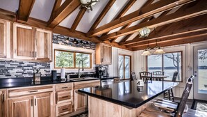 A kitchen with wooden cabinets, a black countertop, and a large island with seating. - Stepaway Vacation Rentals- Lost at Last (St.Germain)