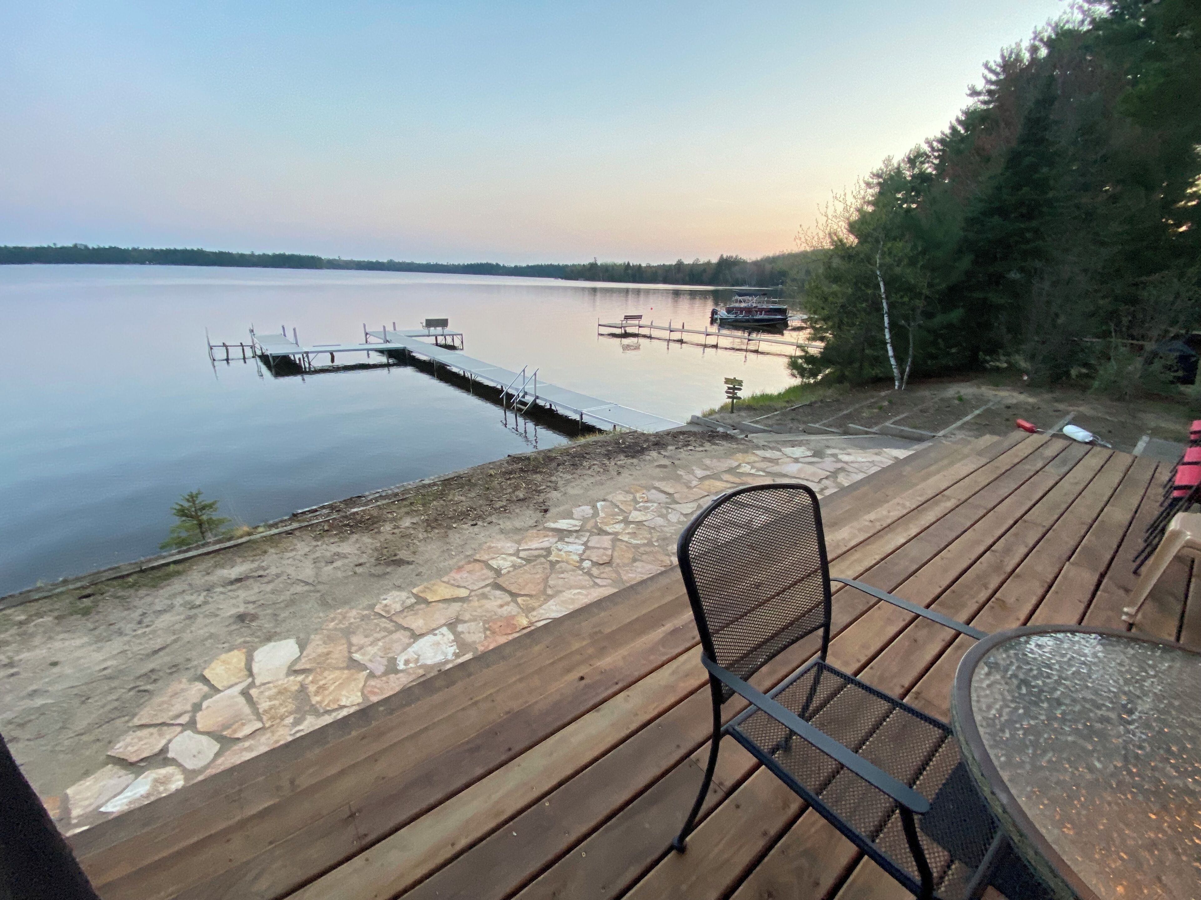 A wooden deck with a stone border, overlooking a calm lake with boats.