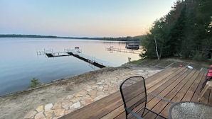A wooden deck with a stone border, overlooking a calm lake with boats. - Stepaway Vacation Rentals- Lost at Last (St.Germain)