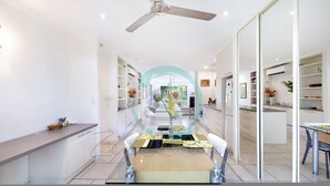 A modern kitchen with white cabinets, a central island, and a dining area with a glass partition. - Zen Treetops Private Pool Outdoor Dining (Larrakeyah)
