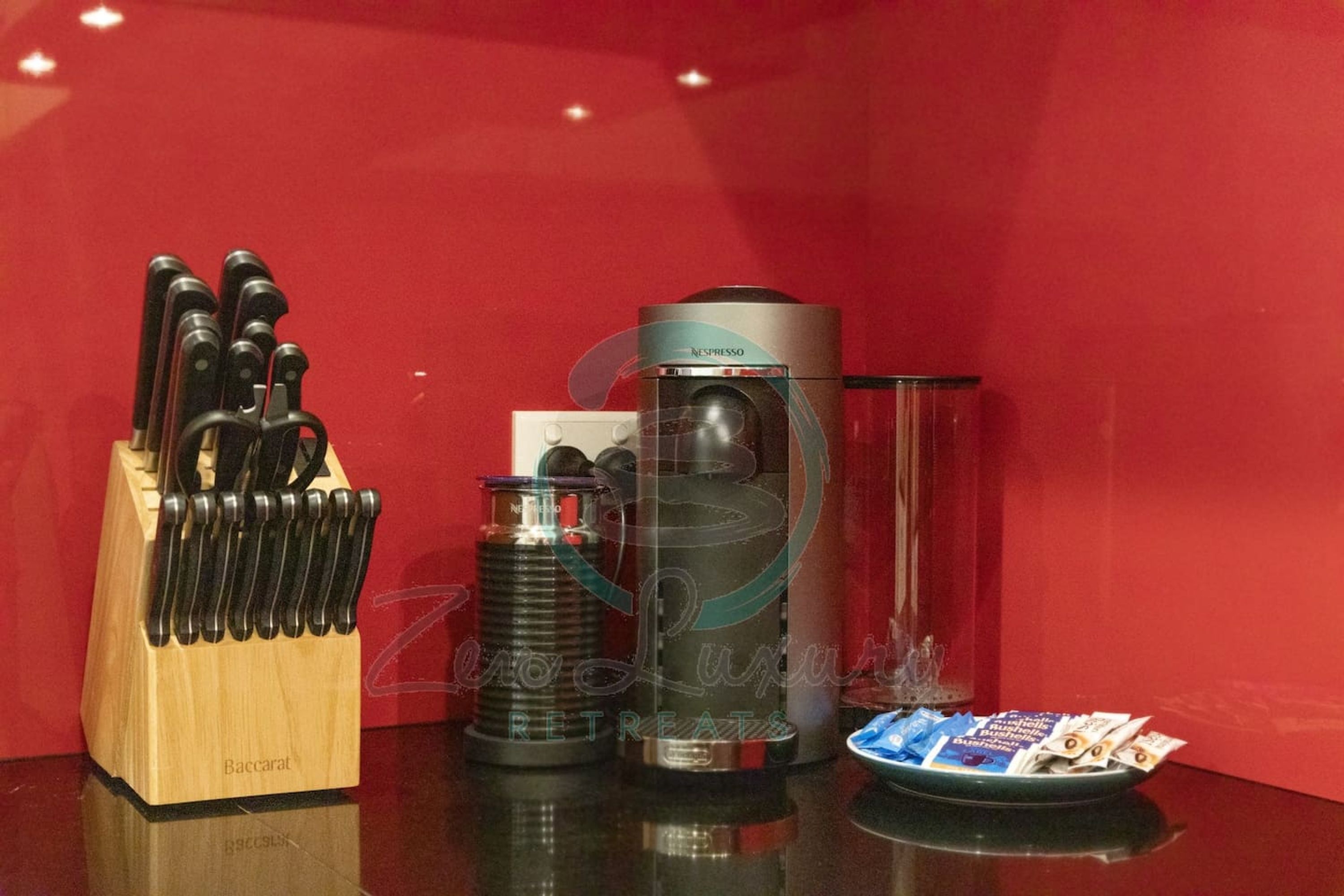 A kitchen counter with a knife block, a coffee machine, a glass container, and a plate with coffee pods.