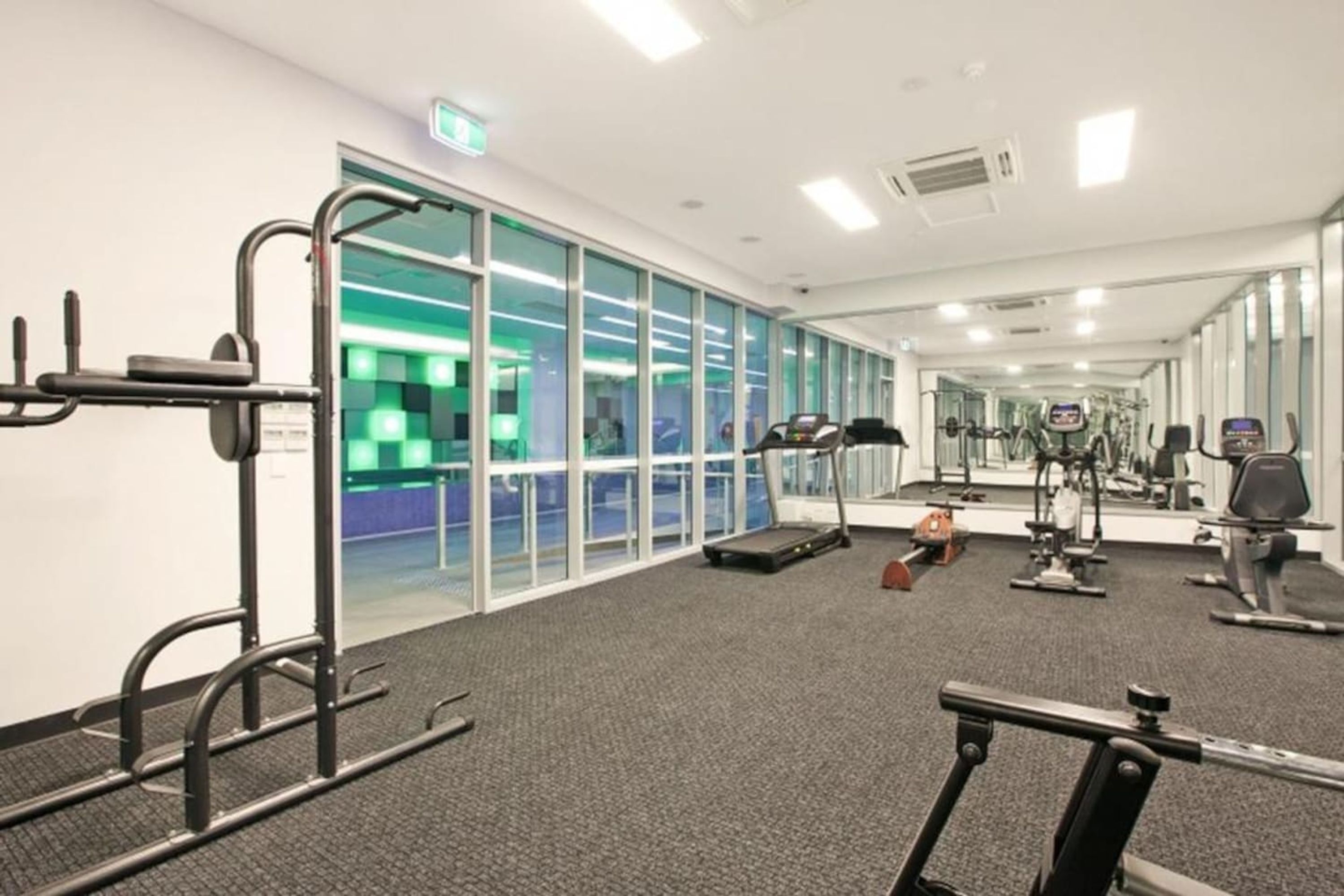 Un gimnasio moderno con máquinas de cardio, equipo de levantamiento de pesas y un espejo grande.