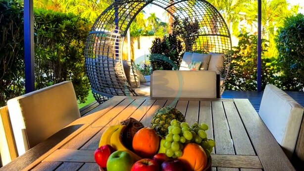 Ein Holztisch mit Obstschale, einer Hängesessel und einer Couch in einem Garten.