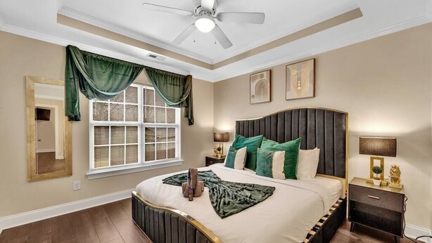 Une chambre à coucher avec un grand lit, un ventilateur de plafond, une fenêtre avec des rideaux, une table de chevet et un miroir.