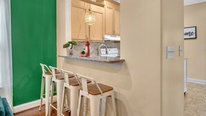 Une cuisine avec des meubles de rangement en bois, un plan de travail en marbre et un luminaire suspendu. On y trouve deux tabourets de bar blancs avec des assises en bois.