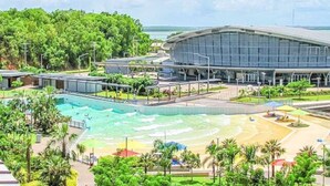 A modern hotel with a large swimming pool, a beach area, and lush greenery. - Rustic Sunset Horizon Oceanview Balcony Dining (Darwin)