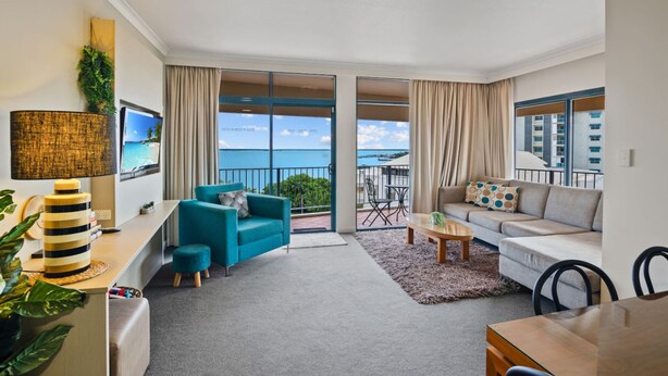 A modern living room with a sofa, armchair, and a dining table. There is a balcony with a view of the ocean. - Rustic Sunset Horizon Oceanview Balcony Dining (Darwin)