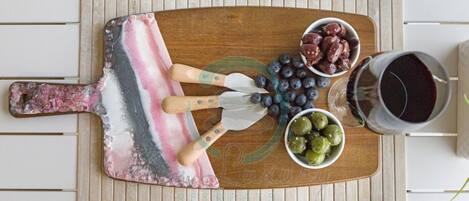 A wooden board with a colorful abstract design, a knife, and bowls of grapes, blueberries, and olives.