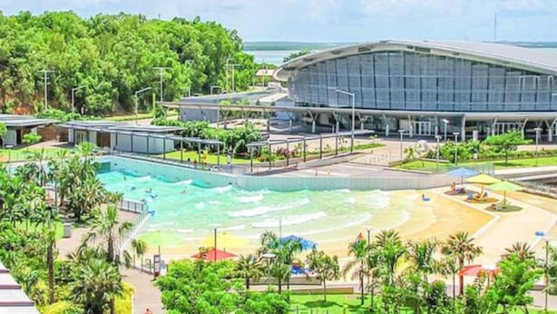Ein modernes Hotel mit großem Schwimmbad, Strandbereich und einer stadiumartigen Struktur.