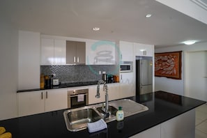 A modern kitchen with white cabinets, a black countertop, stainless steel sink, and a microwave.