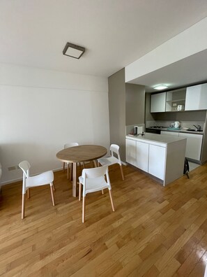 Eine moderne Küche mit weißen Schränken und einem eingebauten Herd. Ein Essbereich mit einem Holztisch und weißen Stühlen ist ebenfalls vorhanden.