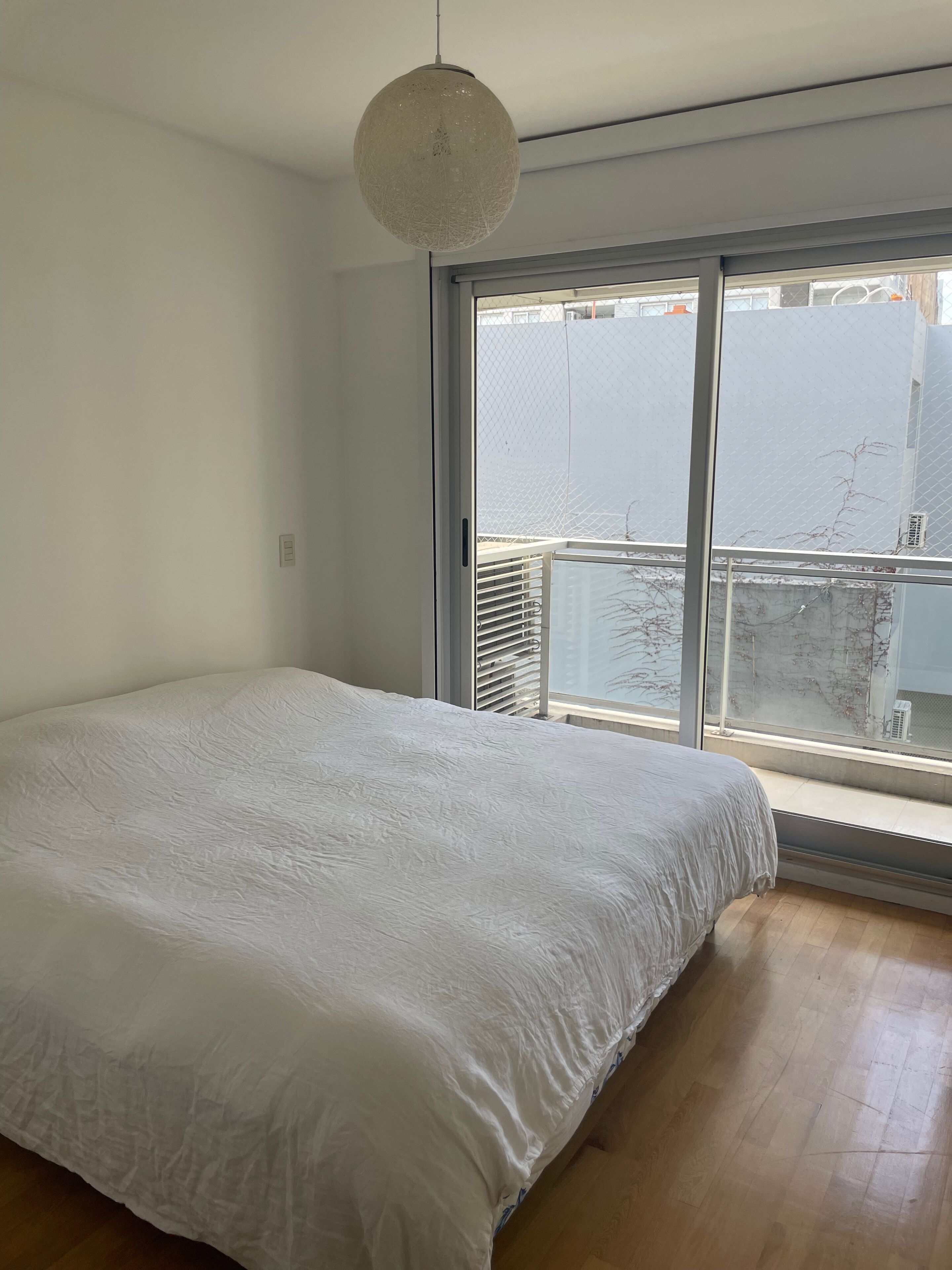 A bedroom with a large bed, a hanging light fixture, and a view through a sliding glass door to an outdoor balcony.