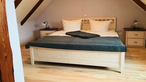 Un dormitorio con cama de madera, mesitas de noche blancas y techo inclinado.